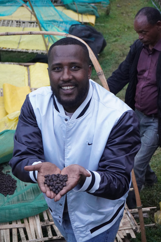 Man holding dried coffee cherries, outdoors with another person in the background.