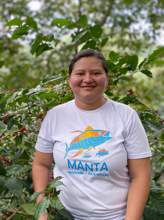 Woman wearing a Manta Manabi Ecuador t-shirt standing among coffee plants.